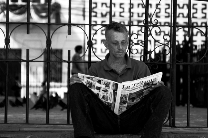 Man reading a newspaper with the headline "Gunmen kill husband of President's secretary". Photo by Gabriel Vallecillo on Flickr, under a Creative Commons license  (CC BY-NC-ND 2.0)